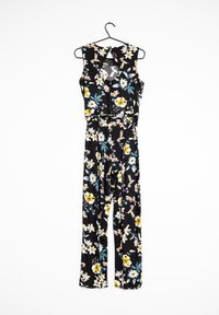 El mono floral presenta un fondo negro, flores amarillas y blancas, un diseño sin mangas y una cintura ajustada con piernas anchas.
