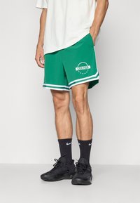 Grønne basketballshorts med et hvidt "CELTICS" logo, kontrasterende hvide side-striber og en elastisk talje.