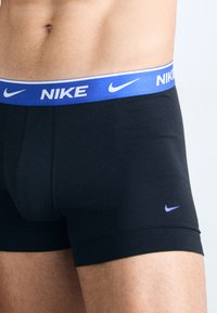 Bóxers negros con bandas elásticas azules que presentan el logo de "Nike" en blanco y un pequeño logo azul cerca del dobladillo. Tejido suave.