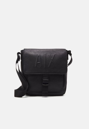 Sac bandoulière en cuir noir avec sangle réglable, rabat avant embossé avec "A|X" et sécurisé par une boucle.