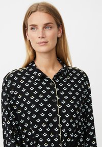 Czarna koszula zapinana na guziki z geometrycznym wzorem w jasnoniebieskim i żółtym kolorze, z kontrastującym jasnym wykończeniem na kołnierzu i listwie.