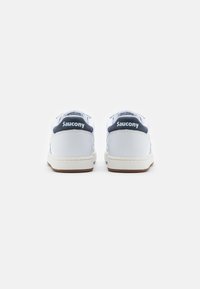 Zapatillas de tenis blancas con acentos azules, punta redondeada, suela de goma texturizada y marca en la parte trasera. Diseño simple y material similar a lona.