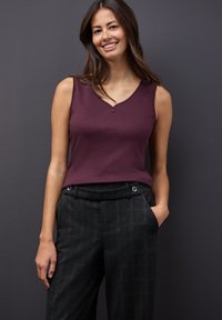 Bordeaux ærmeløs top med V-hals og knapdetalje, parret med højtaljede bukser i sort ternet mønster.