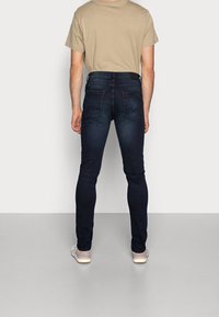 Mörkblå skinny jeans med en jämn textur, med en blekt design och bakfickor med zickzack-sömmar. Bärs med en beige t-shirt.
