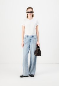 Άσπρη κοντομάνικη μπλούζα, ανοιχτό μπλε παντελόνι με φαρδιά πόδια με σχέδιο με κουκίδες, μαύρα γυαλιά ηλίου και μικρή μαύρη τσάντα χειρός με κοντά χερούλια.