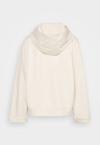 Sudadera con capucha color crema que cuenta con una capucha grande, hombros caídos y puños acanalados. Tela suave con un exterior liso y sin patrones visibles.