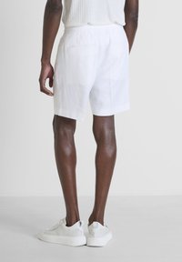Shorts en lin blancs avec une coupe décontractée, dotés d'une taille élastique et de deux poches arrière, associés à des baskets blanches sur une surface lisse.