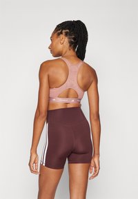 Rosa sport BH med racerback-design og utskåret detalj. Kombinert med høy midje, mørkerøde shorts med hvite sidestreker.