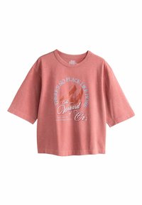 Pink oversized t-shirt made of soft fabric featuring a graphic print with text, red shoes, and a whimsical design related to "The Wizard of Oz."