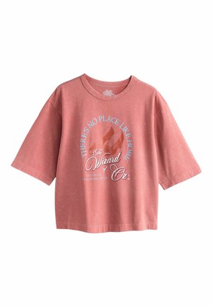 Rosa oversized t-shirt i mjukt tyg med grafiskt tryck som inkluderar text, röda skor och en lekfull design relaterad till "Trollkarlen från Oz."