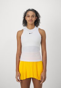 White sleeveless athletic top with a black Nike logo, paired with a pleated yellow skirt. Smooth fabric, fitted design, and vibrant color contrast.