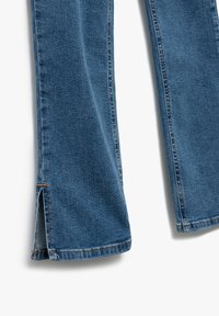 Tummansiniset farkut suoran lahkeen kanssa, joissa on sivuaukot helmassa ja kontrastiväriset tikkaukset. Pehmeä rakenne haalistuneella pinnalla.