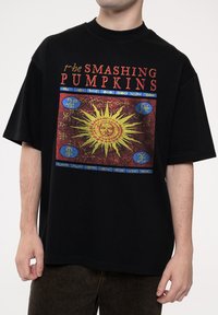 Black oversized t-shirt featuring a colorful graphic print of a sun design and the text "the Smashing Pumpkins" in red and blue.