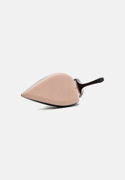 Objeto de cerámica rosa en forma de zapato con puntera afilada y base negra elegante. La superficie es lisa con un acabado brillante. Manija negra adjunta.