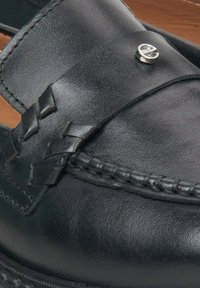 Black leather loafer features a woven strap, decorative silver hardware, and visible stitching details along the edge. Smooth texture overall.