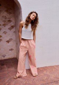 Crop top tricoté blanc associé à un pantalon large rayé rose avec des accents floraux. En arrière-plan, un mur texturé.