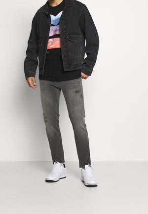 Black denim jacket over a black T-shirt featuring a gradient design; grey distressed jeans; white sneakers with black accents.