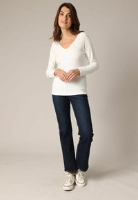 Haut blanc à manches longues en côtelé avec un décolleté en V profond, associé à un jean droit bleu foncé et des baskets blanches avec des accents rouges.