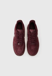Burgundski Nike tenisice s gornjištem od antilopa, perforiranim vrhom, podstavljenim ovratnikom i uparenim vezicama. Ima srebrni logo i gumeni potplat.