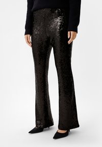 Zwarte paillettenbroek met een uitlopende design, met een glanzende textuur en een glad oppervlak. Draagt met puntige zwarte hakken.