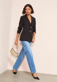 Juodas švarkas su auksiniais mygtukais, derinamas su šviesiai mėlynomis tiesiomis džinsomis. Papuoštas auksiniu delnine ir juodais aukštakulniais.