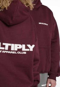 Bordowa bluza z kapturem z białym napisem "MULTIPLY" i logo "APPAREL CLUB". Kieszeń kangurka, długie rękawy i miękka faktura.