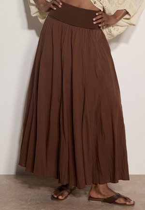 Brown wide-leg pants worn with dark brown sandals, paired with a cream textured sweater, hands resting on hips.