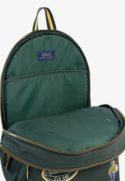 Temno zelen nahrbtnik Polo Ralph Lauren odprt, da pokaže oblazinjeni predel za prenosnik in notranji žep, z ročajem z žakardnim vzorcem in podrobnostmi z zadrgo.