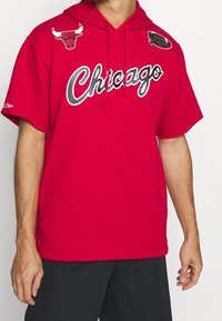 Sudadera con capucha roja con "Chicago" en texto blanco, presentando logotipos del equipo en negro y rojo en los hombros. Fabricada con una tela suave y casual.