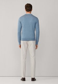 Lichtblauwe trui met lange mouwen en een ronde hals, gecombineerd met lichtbeige broek. De stof lijkt zacht en glad.