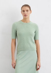 Maglione verde a maniche corte con un knit testurizzato, scollatura e orlo a coste, abbinato a una gonna liscia e aderente dello stesso colore.