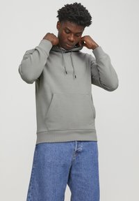 Gray hoodie with a kangaroo pocket, adjustable drawstring hood, ribbed cuffs, and hem. Paired with blue denim jeans.