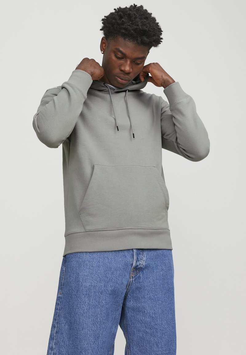 Gray hoodie with a kangaroo pocket, adjustable drawstring hood, ribbed cuffs, and hem. Paired with blue denim jeans.