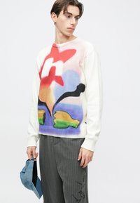 Πλεκτό πουλόβερ σε λευκό με πολύχρωμο αφηρημένο σχέδιο που περιλαμβάνει κόκκινες, μπλε, μαύρες και πράσινες αποχρώσεις. Ριμπ μανσέτες και τελείωμα.