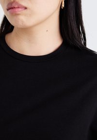 Black cotton t-shirt with a round neck, featuring a smooth texture and plain design, worn by a person with earrings visible.
