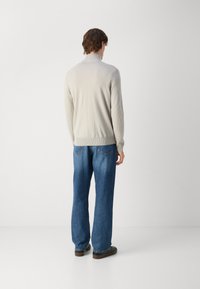 Lys grå strikkegenser med høy krage, ribbestrikkede mansjetter og liv, brukt med løstsittende blå jeans og brune sko.