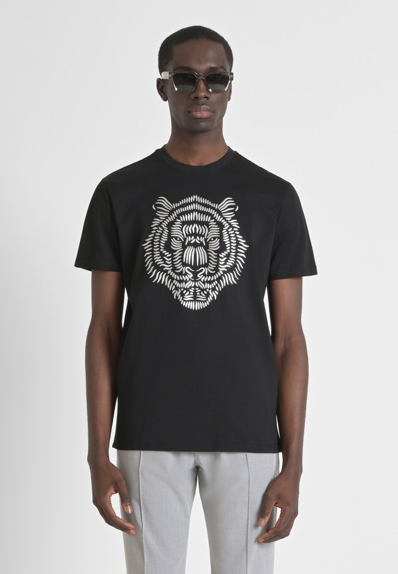 Camiseta negra de manga corta con un diseño gráfico de un tigre blanco en el frente. Tejido suave con escote redondo. Combinada con pantalones grises claros.
