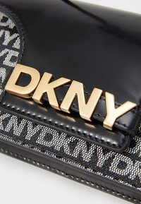 Portefeuille en cuir verni noir avec un motif texturé gris et noir, accentué par un logo doré "DKNY" sur le devant.