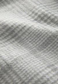 Harmaa kuviollinen kangas, jossa on pehmeä, teksturoitu pinta, jossa on hienovarainen ruudukko-kuvio ja lempeät aaltoilevat taitteet.}}