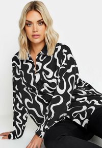 Camicia a maniche lunghe con motivo astratto in bianco e nero, con chiusura frontale a bottoni e una singola tasca sul petto. Tessuto morbido con vestibilità comoda.