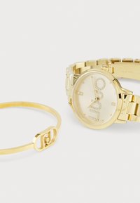 Gold watch with a polished case, designed with studded hour markers and a linked metal band. Accompanied by a minimalistic gold bracelet.