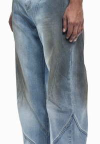 Svetlo modre kavbojke iz denim materiala z geometričnim vzorcem, značilno bledim učinkom in izrazitim šivom ob šivih in žepih.