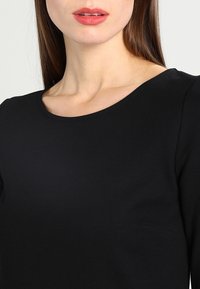 Musta toppi pyöreällä kaula-aukoilla ja lyhyillä hihoilla. Sujuva pinta ja tiukka muotoilu, jossa on sivusaumapussi.