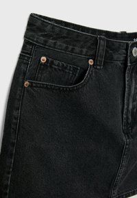 Jeans in denim nero con una vestibilità classica, dotati di tasca frontale, accessori in tono rame e cuciture visibili lungo il cinturino e le cuciture.