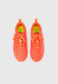 Jasnopomarańczowe buty sportowe z oddychającą siateczkową cholewką, zdobione białymi kwiatowymi wzorami, z wyściełanym kołnierzem i płaskimi sznurowadłami.