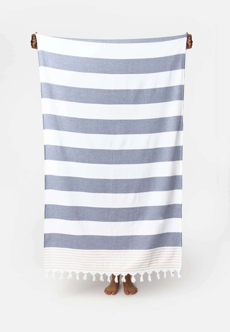 Coperta in cotone con strisce orizzontali blu e bianche, rifinita con un bordo cremoso testurizzato e con frange nella parte inferiore.