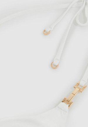 Valge bikiinivöö ülemine osa, millel on reguleeritavad rihmad kuldse tooni riistvara ja sile tekstuur. Detailide hulka kuuluvad dekoratiivne klamber ja sidumismehhanism.