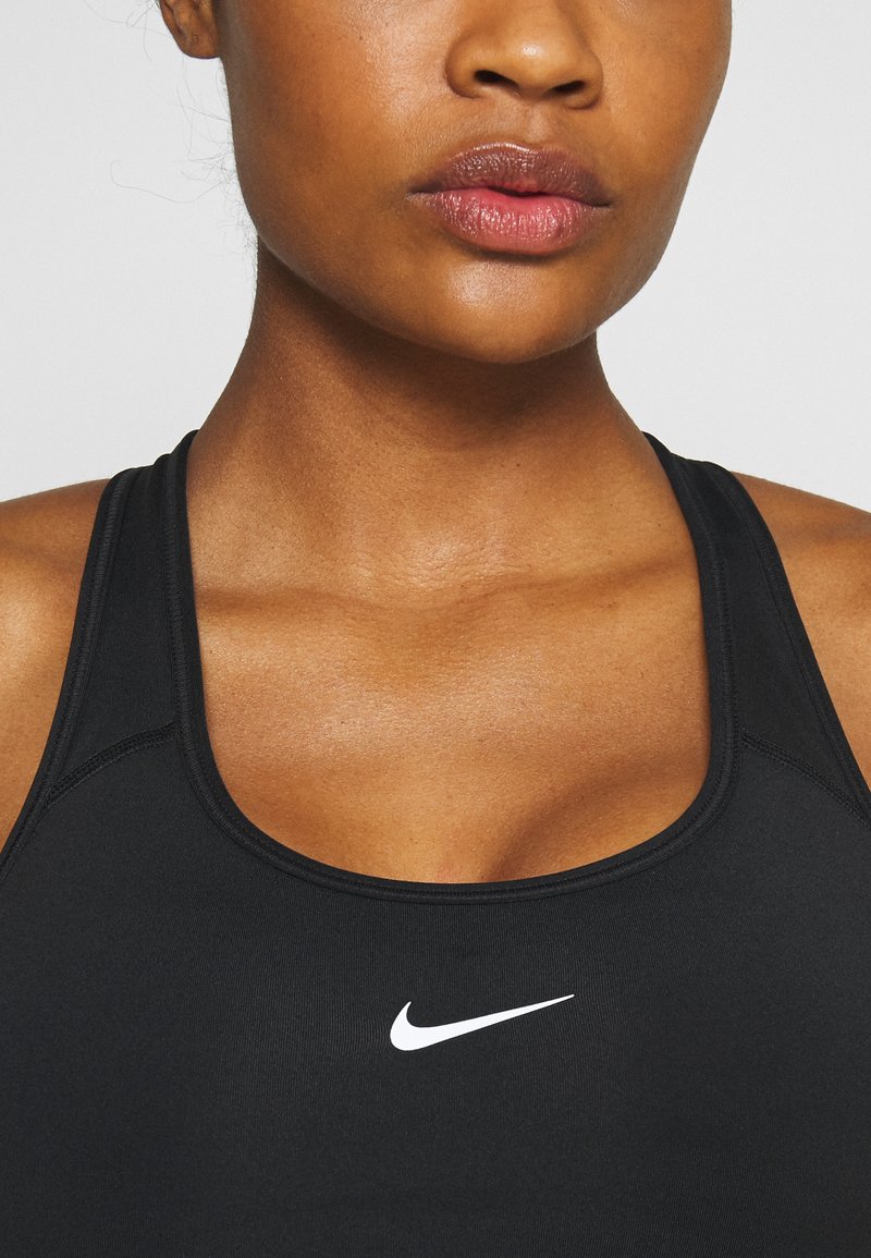 Soutien-gorge de sport noir au design épuré, fabriqué en matériau doux, avec un logo Nike blanc à l'avant et une coupe dos nageur.