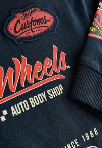 Granatowa bluza z czerwonym haftem "Hot Wheels Customs" oraz białym napisem "AUTO BODY SHOP" i "SINCE 1968" z przodu, z prążkowanymi mankietami.