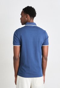 Mørkeblå polo shirt har et klassisk design med krave, korte ærmer og hvide detaljer ved kraven og ærmeslutterne.